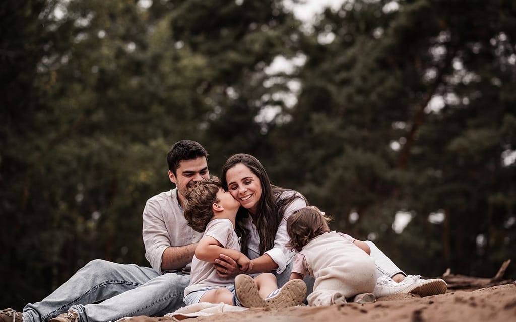Familien mit zwei Kindern beim Fotoshooting in Nürnberg auf der Sanddüne. Sie sitzen zusammen im Sand und lachen.
