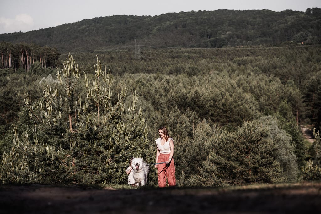 Mutter läuft mit ihrem weißen Hund klein in der weiten Sanddünenlandschaft des Fränkischen Dünenwegs bei Nürnberg.