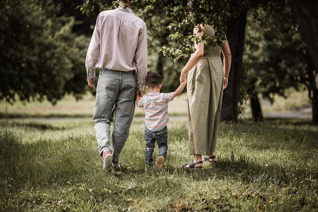 Papa, Mama und Sohn halten sich an den Händen und laufen über eine Wiese inmitten von Apfelbäumen.