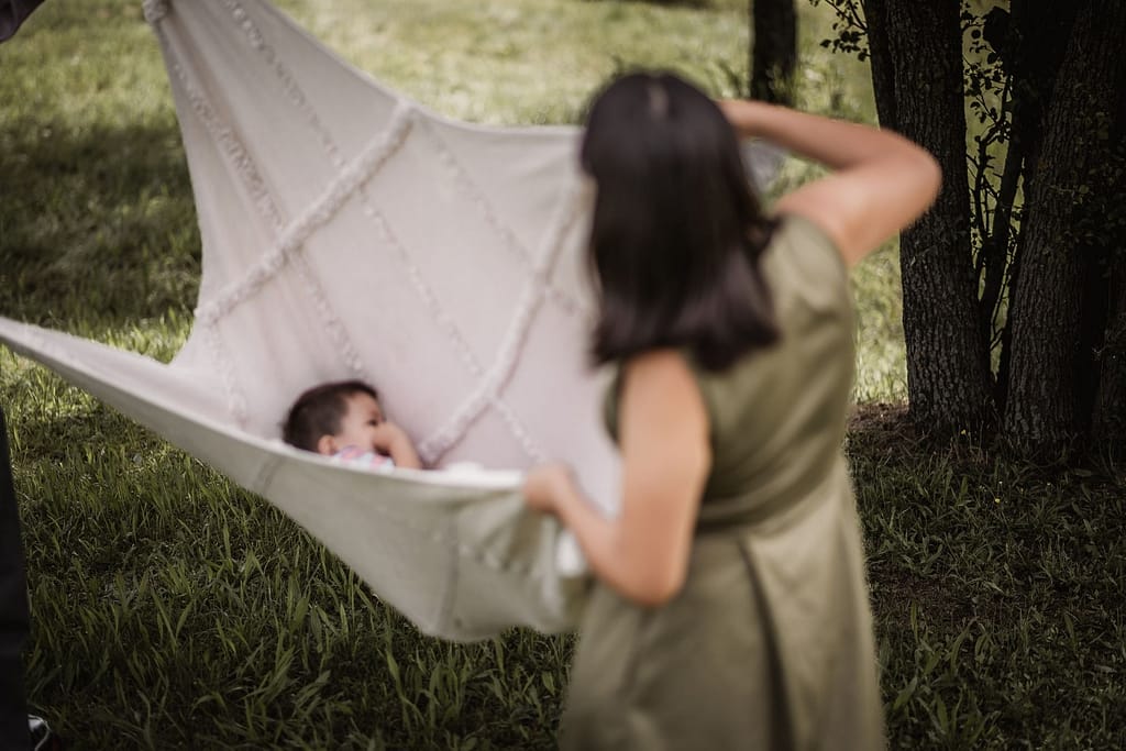 Mama und Papa halten eine cremefarbene Picknickdecke als Schaukel. In der Decke liegt ihr 3-jähriger Sohn, der sich beim Familienshooting schaukelnlässt.