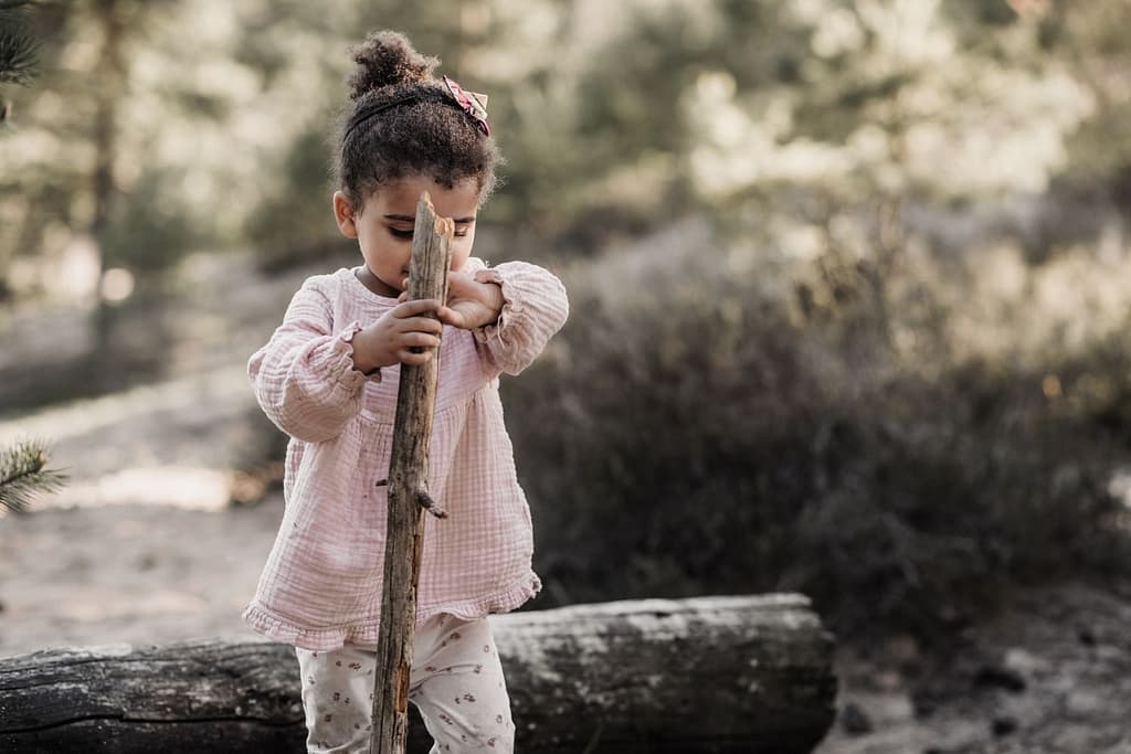 Kleines Kind in rosa Oberteil steht draußen am fränkischen Dünenweg und hält einen großen Ast wie einen Wanderstock bei einem Fotoshooting in Nürnberg und Fürth.