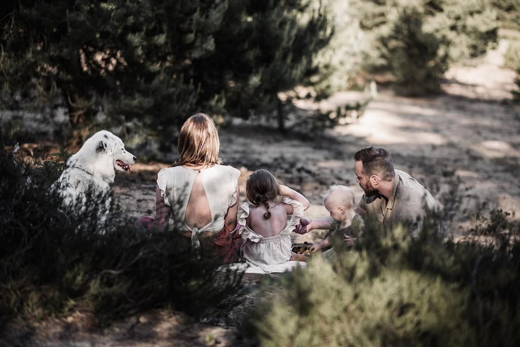 Familie von hinten auf bei einem Picknick auf den Sanddünen am fränkischen Dünenweg. Mama, Papa, zwei kleine Kinder und 2 Hunde ruhen sich entspannt aus.