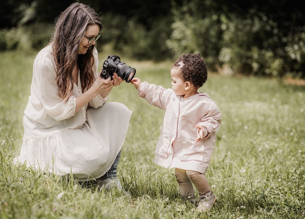 Familienfotografin mit Kamera und kleinem Kind auf einer grünen Wiese