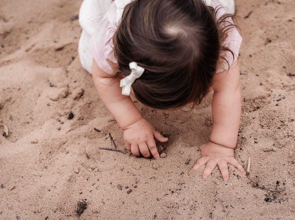 Kleinkind mit Schleife im Haar an der Sanddüne in Erlenstegen bei Nürnberg buddelt mit den Händen im Sand.