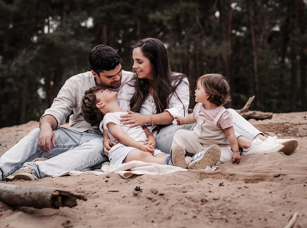 Familien mit 2 kleinen Kindern sitz auf einer cremefarbenen Picknickdecke auf einer Sanddüne.