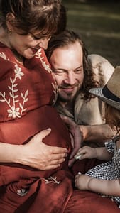 Familie mit werdender Mama und kleinem Kind auf einer Picknickdecke im Park