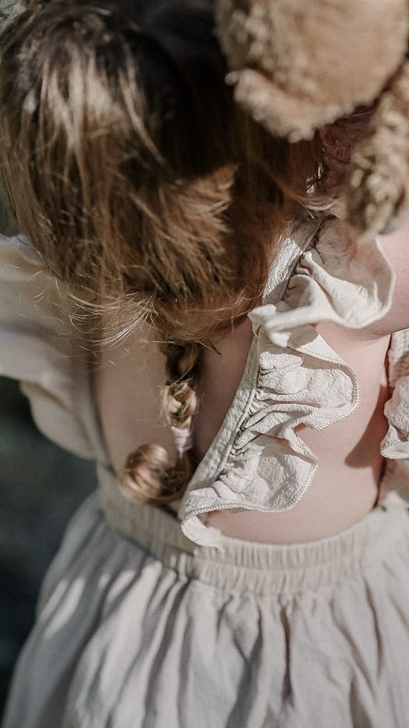 Nahaufnahme vom Rücken eines kleinen Mädchens mit geflochtenem Zopf in einem Leinenkleid.