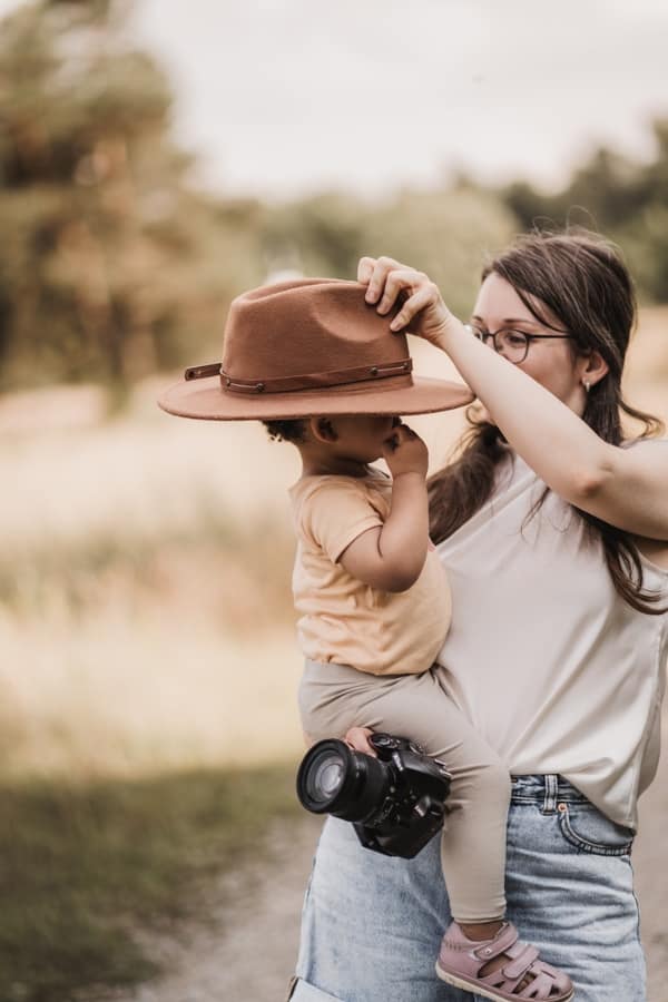 Stefie - Familienfotografin in Nürnberg, Fürth und Umgebung. Auf dem Foto ist die Fotografin mit einem kleinen Mädchen auf dem Arm zu sehen. Sie hält ihre Kamera und setzt dem Kind einen Hut auf.
