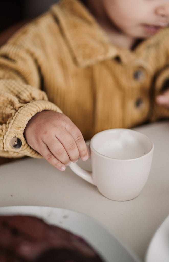 Nahaufnahme einer KLeinkindhand bei einer Homestory. Sie hält eine kleine Tasse Babyccino.