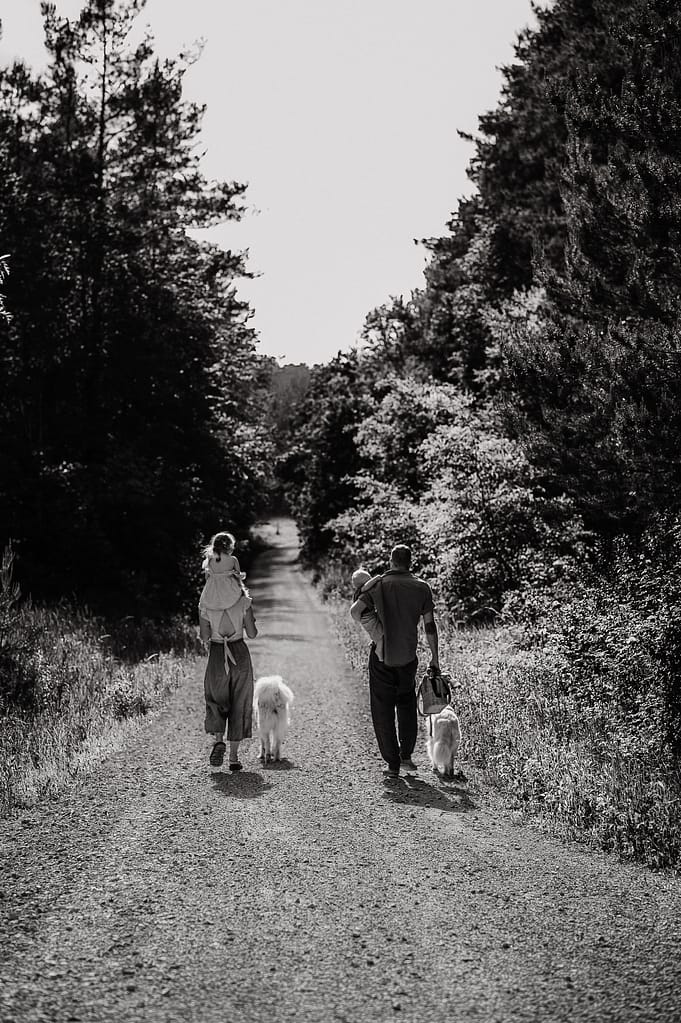 Familie geht mit ihrem weißen Hund einen Waldweg am Fränkischen Dünenweg bei Nürnberg entlang, Schwarzweiß-Aufnahme von hinten.