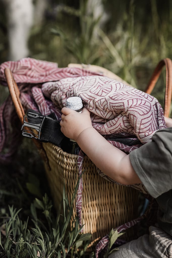 Kinderhand greift nach der Decke in einem geflochtenen Picknickkorb im Gras.