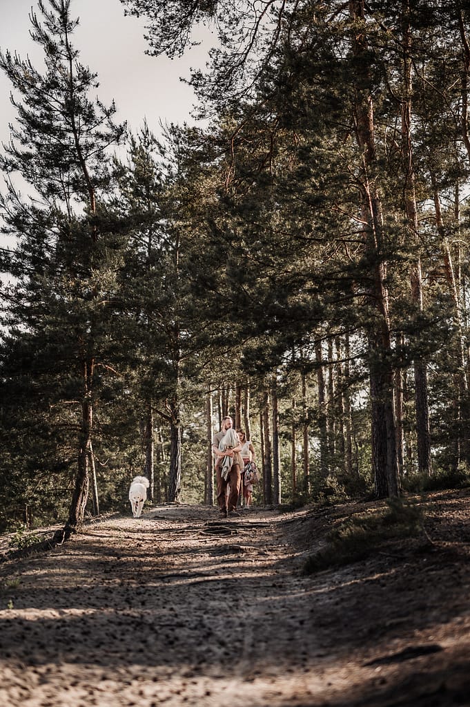 Familie spaziert mit Hund einen sonnendurchfluteten Kiefernwaldweg entlang – Familienshooting am Fränkischen Dünenweg.