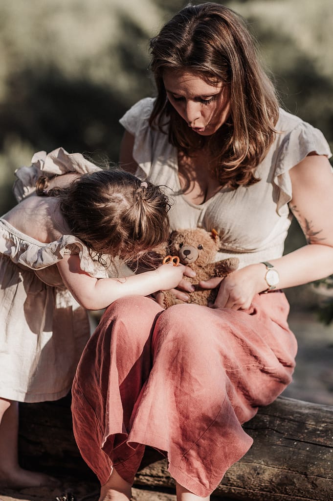 Mutter und Tochter schmiegen sich mit dem Teddybären aneinander.