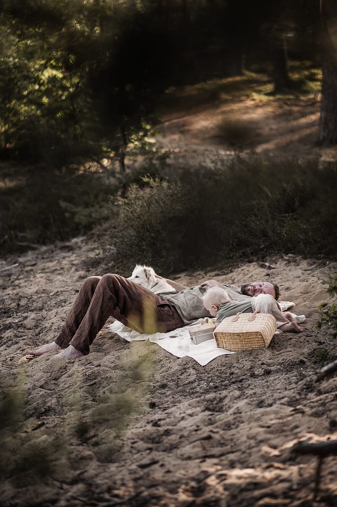 Familie sitzt zusammen auf einer Picknickdecke im Sand des Dünenwegs.