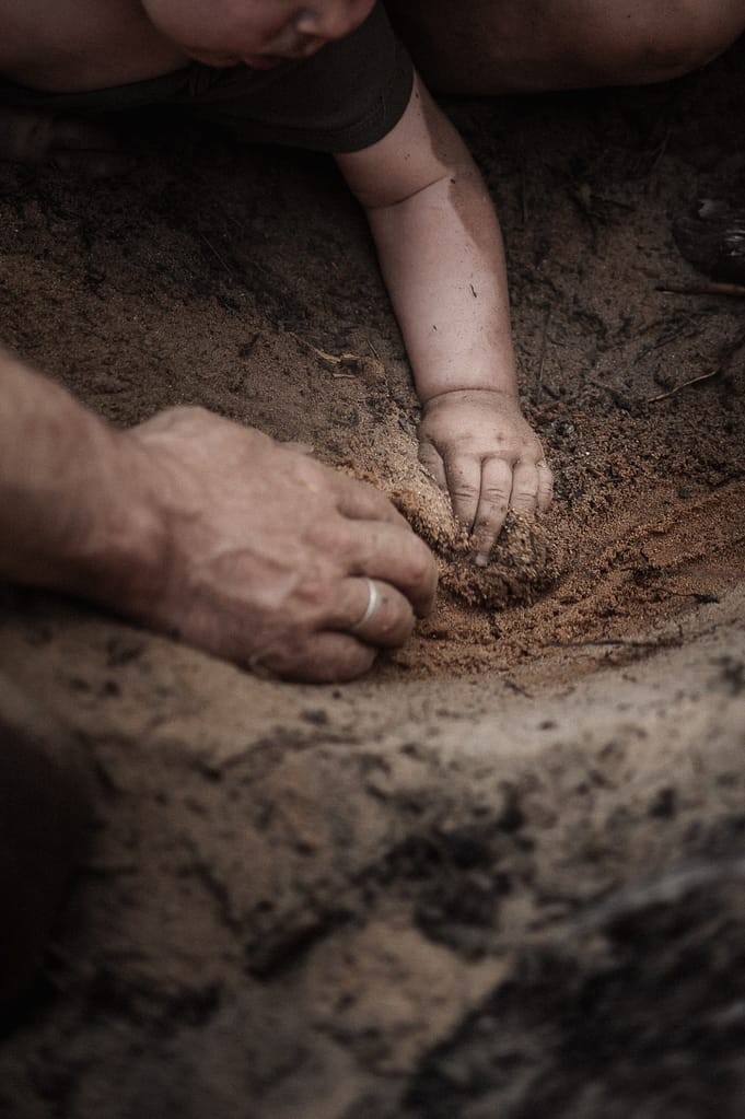 Große und kleine Hände graben gemeinsam im Sand – Nahaufnahme von Vater und Baby beim Familienfotoshooting am Dünenweg bei Nürnberg Fürth.