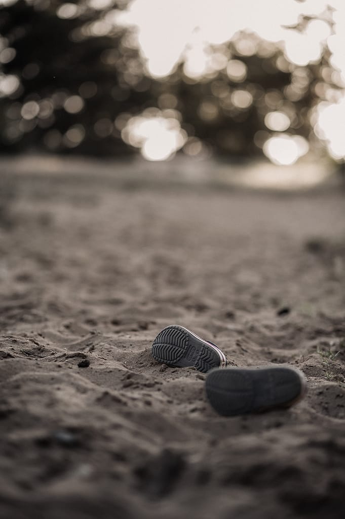 Ein einzelner Kinderschuh liegt im Sand, im warmen Gegenlicht des Abends.
