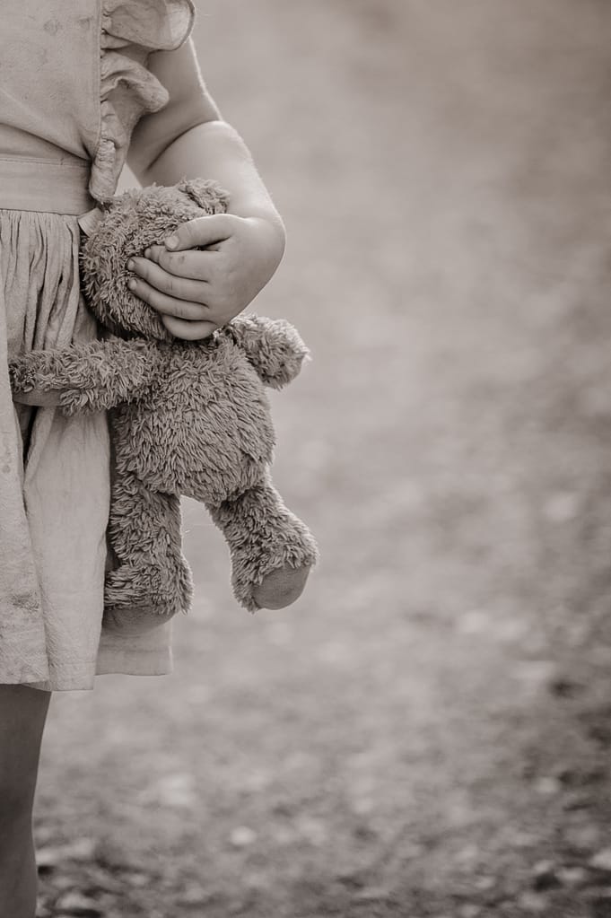 Kleine Hände umklammern den Teddybären, Schwarzweiß-Detailaufnahme.