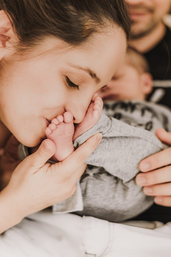 Mama küsst Neugeborenenfüße in ihrem Zuhause