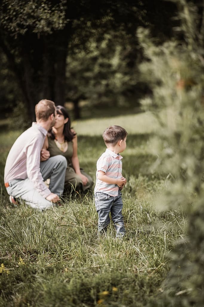 Mama, Papa und kleiner Sohn knien in einer schonen Wiese inmitten von Apfelbäumen.