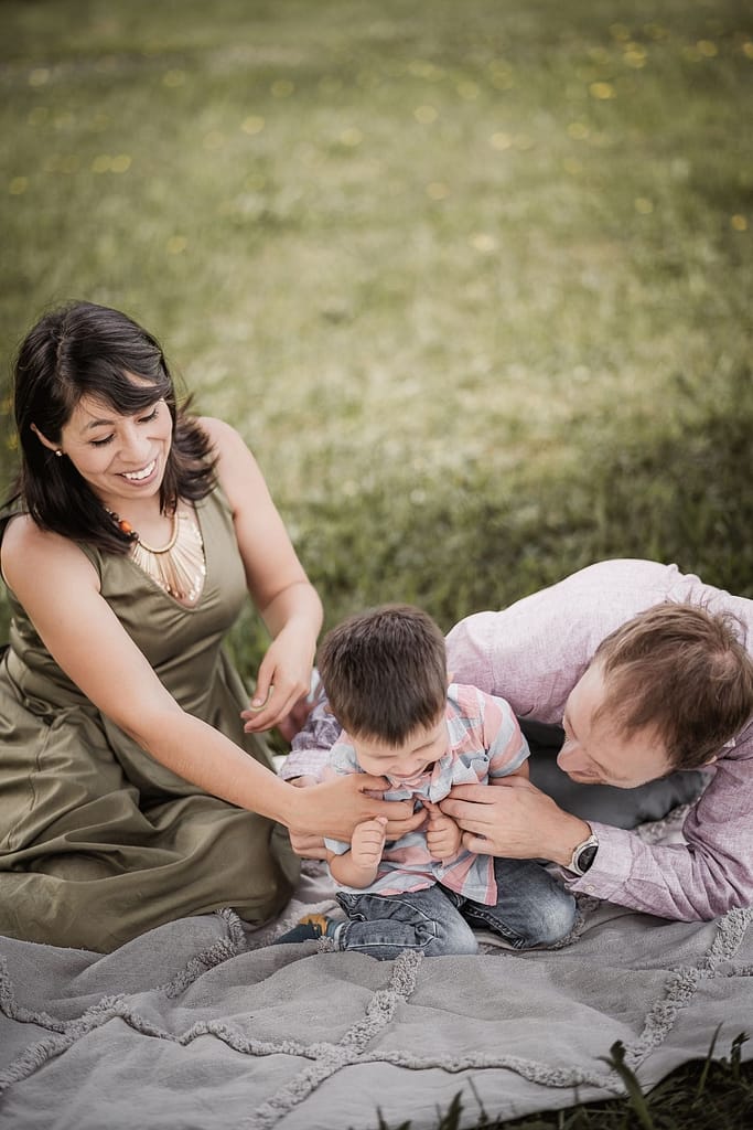 Beim Familienshooting lachen Mama und Papa mit ihrem 3-jährigen Sohn. Der Junge wird von seinen Eltern durchgekitzelt und strahlt.