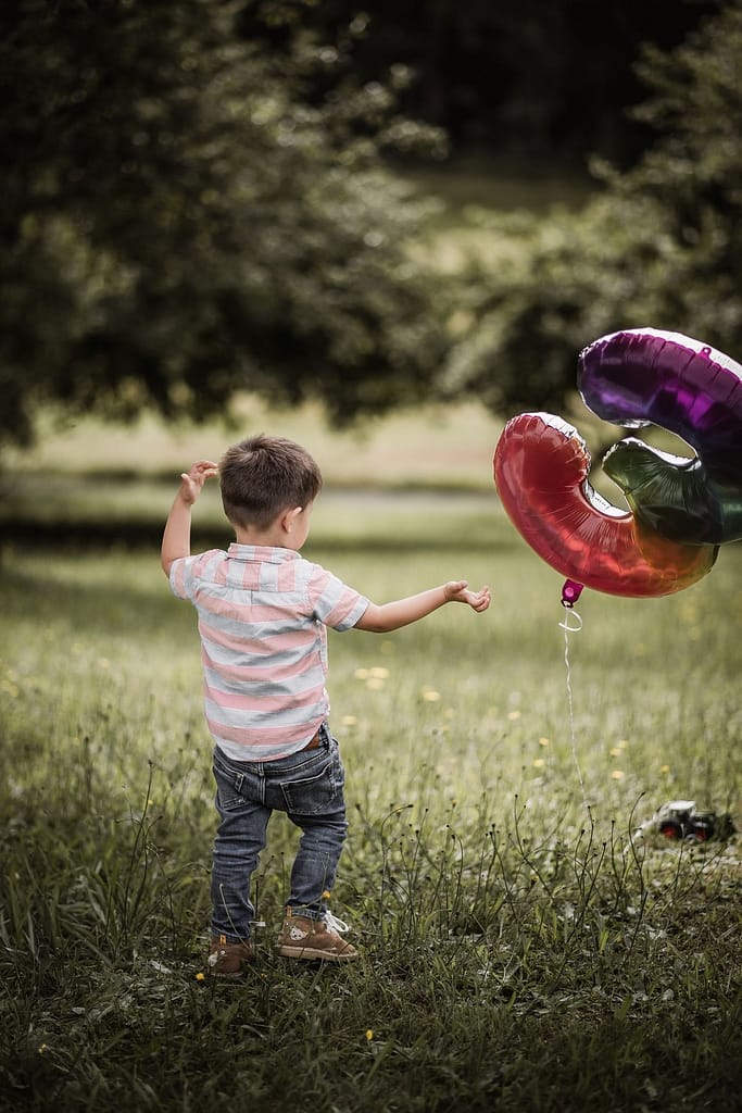 3-jähriger Junge beim Familienshooting spielt auf einer Wiese mit einem Folienballon mit der Zahl 3.