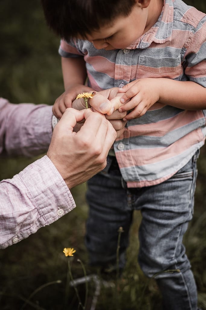 Nahaufnahme von Papa und Sohn beim Familienshooting. Sie haben ein Löwenzahl in mit Marienkäfer in der hand.
