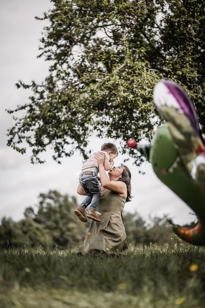 3-jähriger Junge beim Familienshooting rennt über eine Wiese zu seiner Mama. Diese hebt ihn lachend in die Luft.