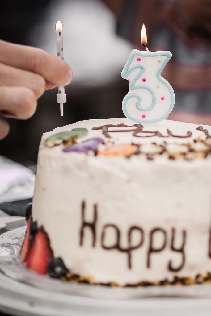 Nahaufnahme eines Geburtstagskuchens beim Familienshooting. Eine Hand steckt Kerzen auf die Torte.
