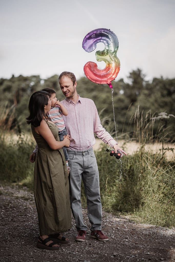 Familie mit Kleinkind und einem schwebenden Ballon mit der Zahl 3.
