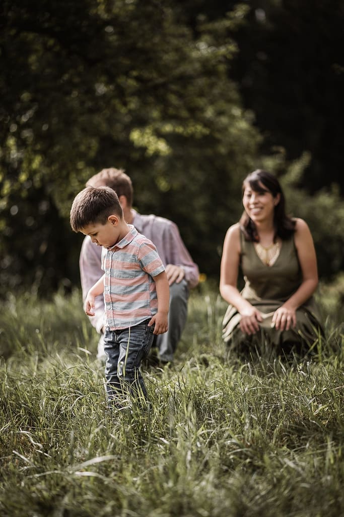 Mama, Papa und kleiner Sohn knien in einer schonen Wiese inmitten von Apfelbäumen.