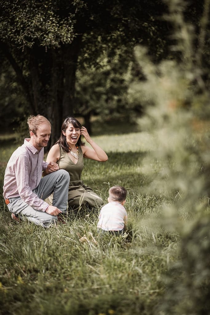 Mama, Papa und kleiner Sohn knien in einer schonen Wiese inmitten von Apfelbäumen.