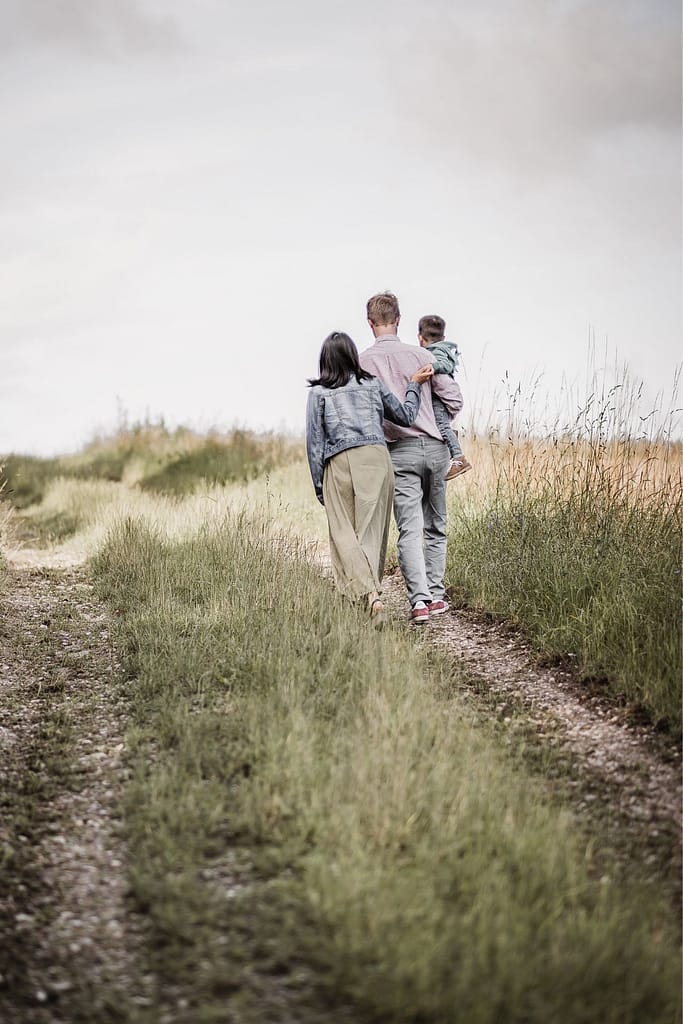 Familienfoto mit Kleinkind. Mama, Papa und Sohn laufen auf einem Feldweg weg von der Kamera. Sie sind beim Familienshooting bei Nürnberg in der Natur unterwegs.