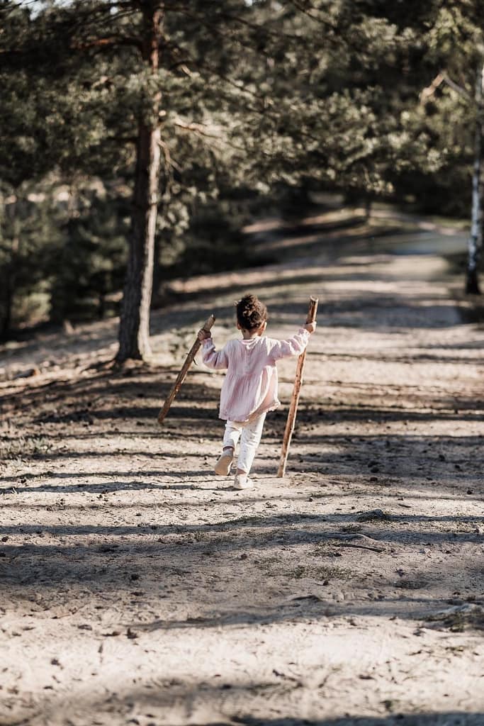 Kleines Mädchen von hinten fotografiert mit zwei Ästen als Wanderstöcken auf dem fränkischen Dünenweg