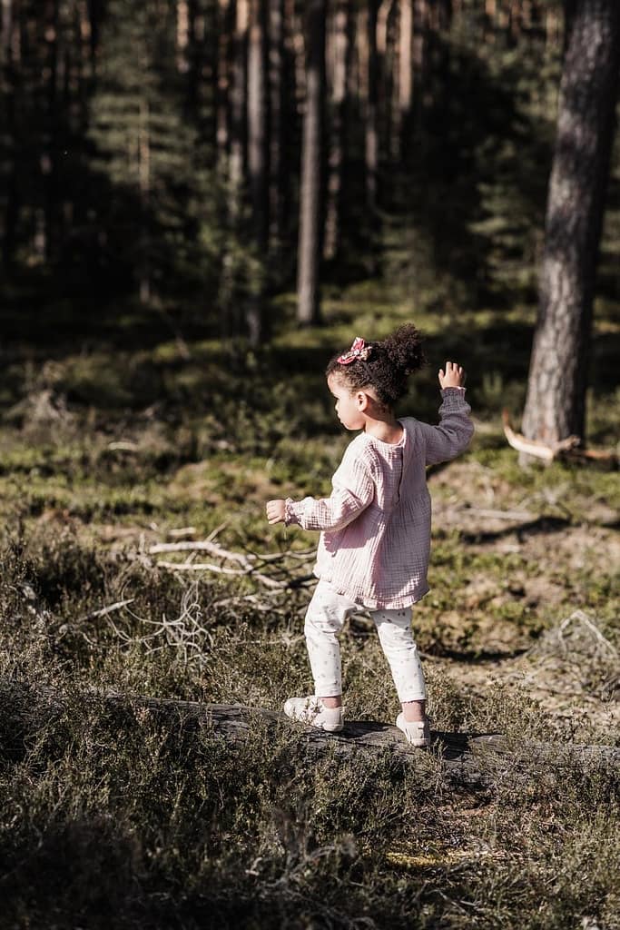 Kleines Mädchen in heller Kleidung balanciert auf einem umgefallenen Baumstamm im Wald am fränkischen Dünenweg