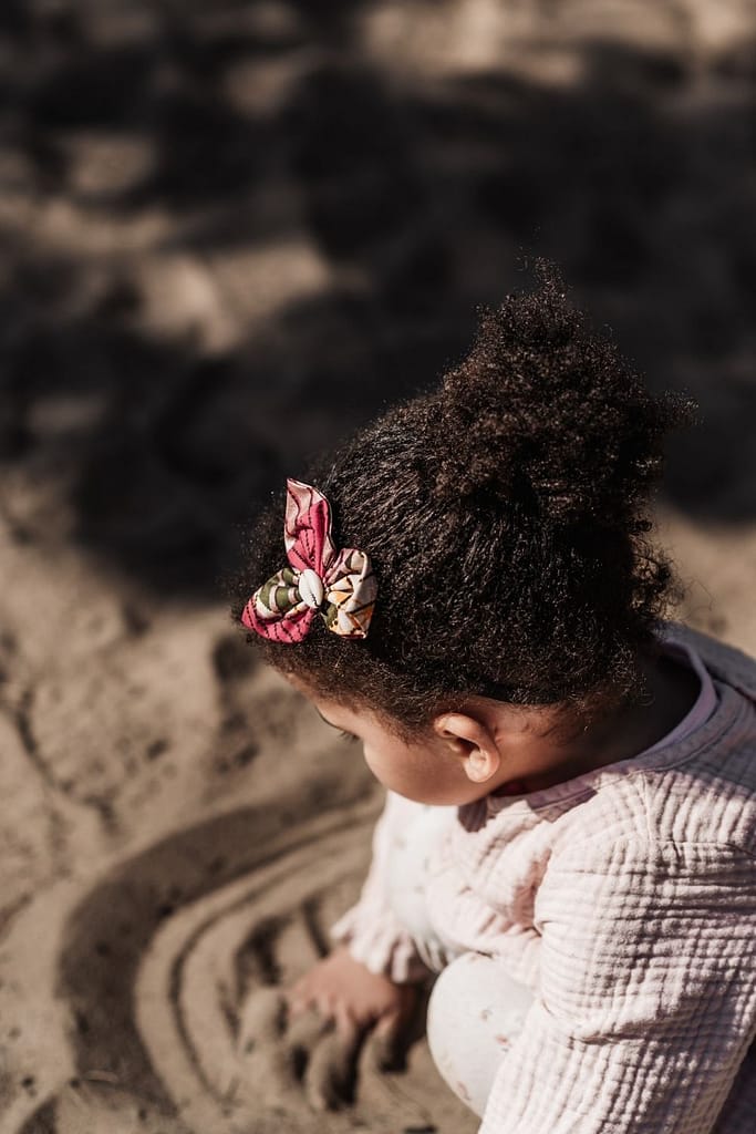 Kleines mädchen von oben fotografiert hockt im sand und macht mit den Händen Rillen in den Sand
