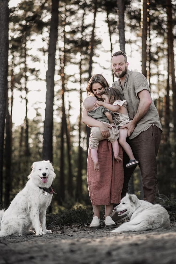 Familie im Wald Das sind die Momente, die ich meine. Die man nicht plant. Die einfach passieren, wenn man sich die Zeit lässt. Die Eltern halten ihre 2 Kinder auf den Armen,während auf beiden Seiten die Hunde daneben sitzen oder liegen.