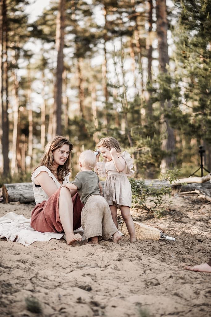 Mama verzieht lachend das Gesicht, während sie ihrem einjährigen Sohn Seifenblasen aus den Augen wischt. Die große Schwester steht daneben und schaut zu. Die Familie sitzt im goldenen Licht auf einer Sanddüne am fränkischen Dünenweg.