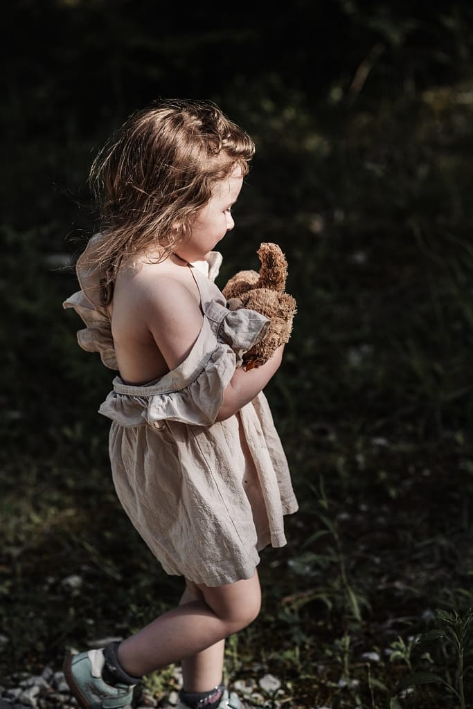 KLeines Mädchen läuft mit ihrem Teddy im Arm auf einem kiesigen Weg beim Familienshooting am fränkischen Dünenweg.