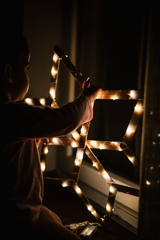 Warem Lichter an einem Weihnachtsstern mit einem kleinen Kind bei, das den Stern hält. Das Bild ist sehr dunkel, mit reflektierenen warmen Lichtern am Stern.