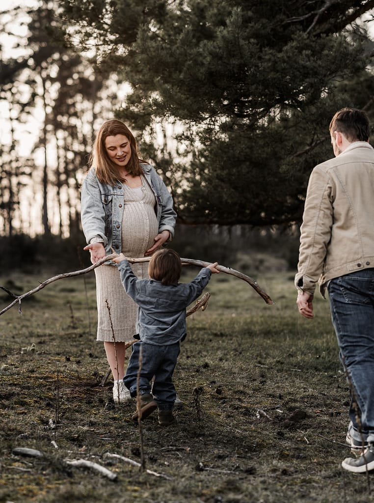 Familie mit kleinem Sohn und schwangerer Mama im Wald. Sie spielen zusammen. Der Sohn bringt Mama einen großen Ast.