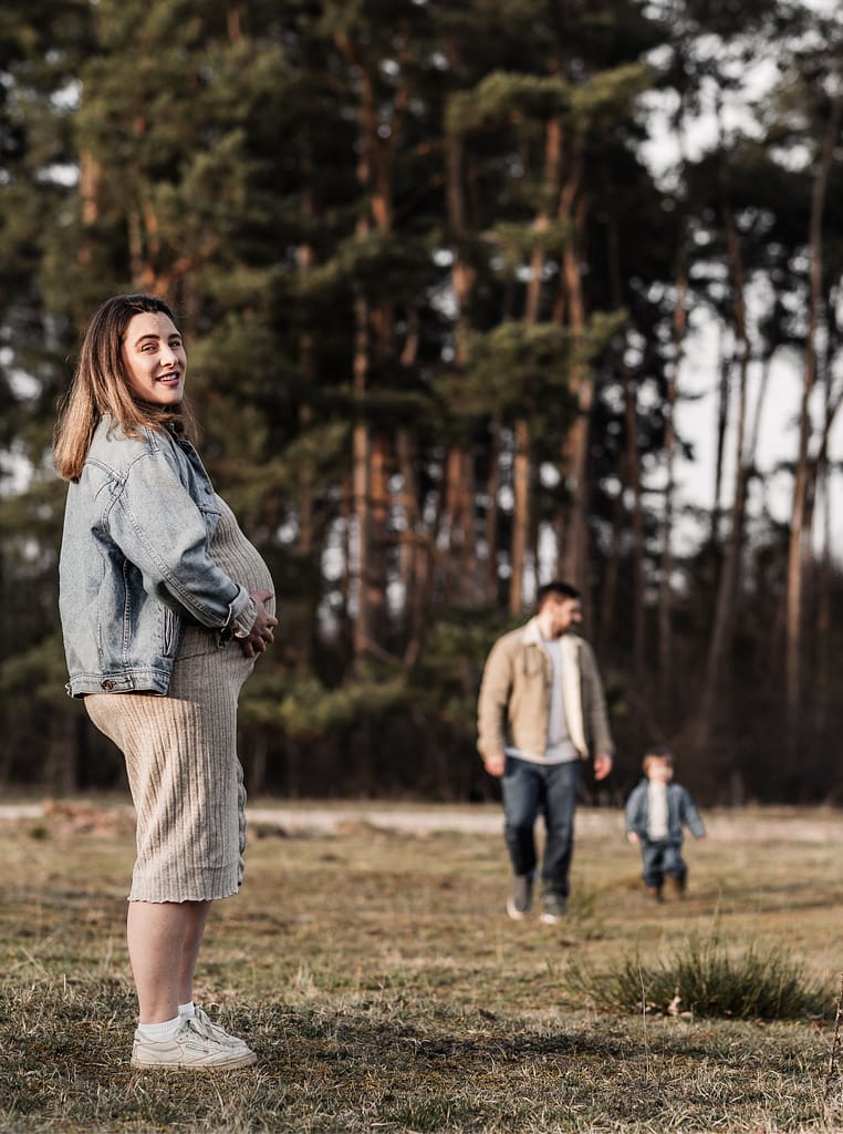 Familien draußen in der Natur beim Familien und Babybauchshooting. Sie genießen die gemeinsame Zeit auf einer Wiese umgeben von Wald.