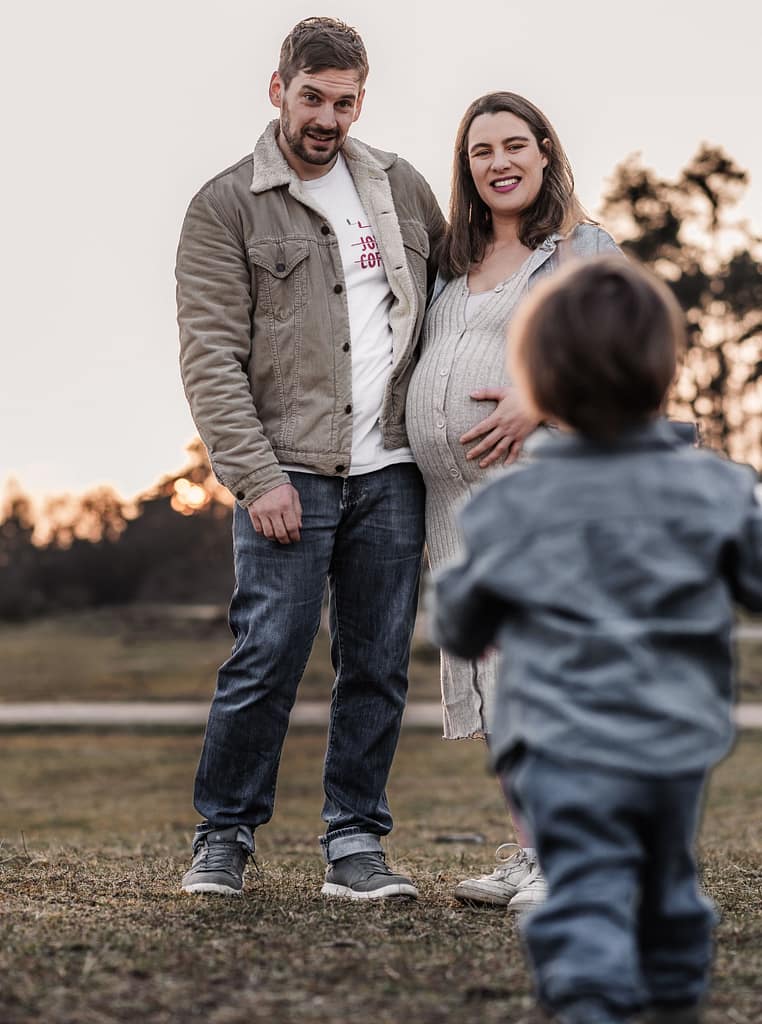 Familien draußen in der Natur beim Familien und Babybauchshooting. Sie genießen die gemeinsame Zeit auf einer Wiese umgeben von Wald.