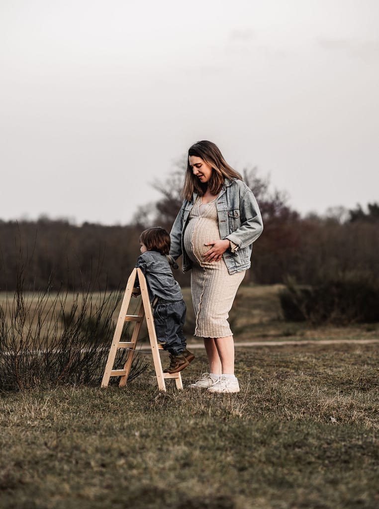 Mama mit Sohn draußen in der Natur beim Familien und Babybauchshooting. Sie genießen die gemeinsame Zeit auf einer Wiese umgeben von Wald.