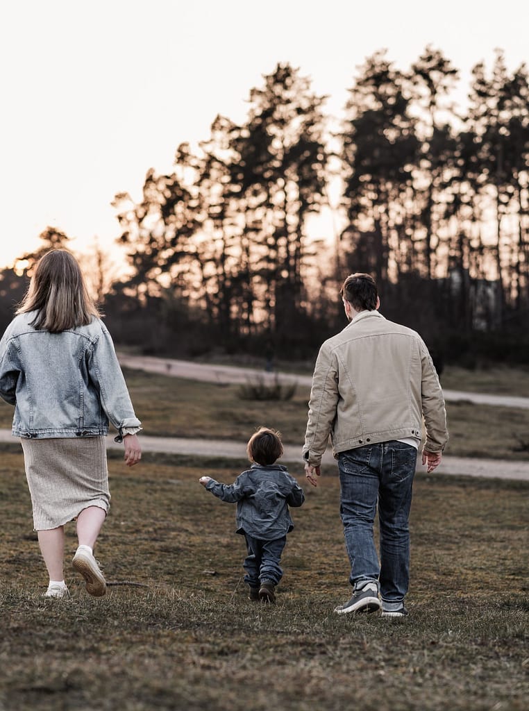 Familien draußen in der Natur beim Familien und Babybauchshooting. Sie genießen die gemeinsame Zeit auf einer Wiese umgeben von Wald.