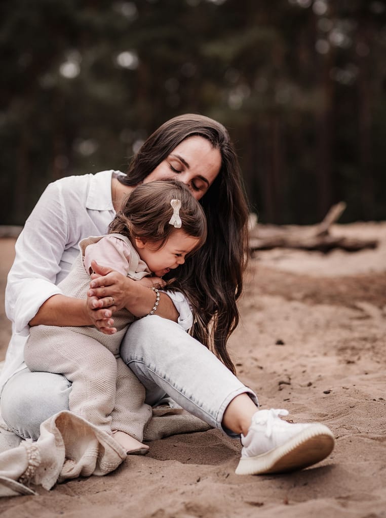 Mama sitz mit kleinem Kind auf einer Sanddüne und knuddelt es beim Familienshooting Nürnberg.